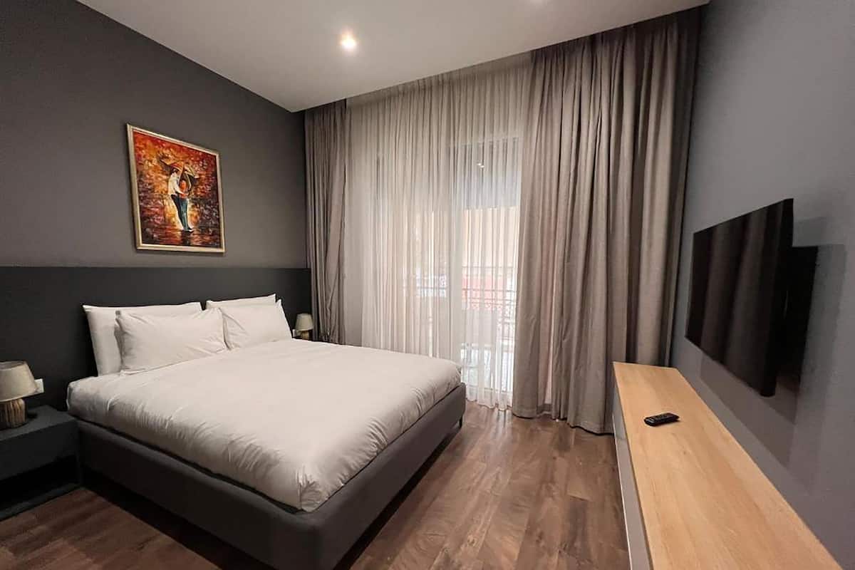 A modern bedroom with a large bed, a TV mounted on the wall, and a window with curtains.