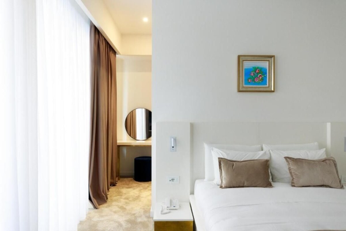 A hotel room with a bed, a bedside table, a mirror, and a painting on the wall.