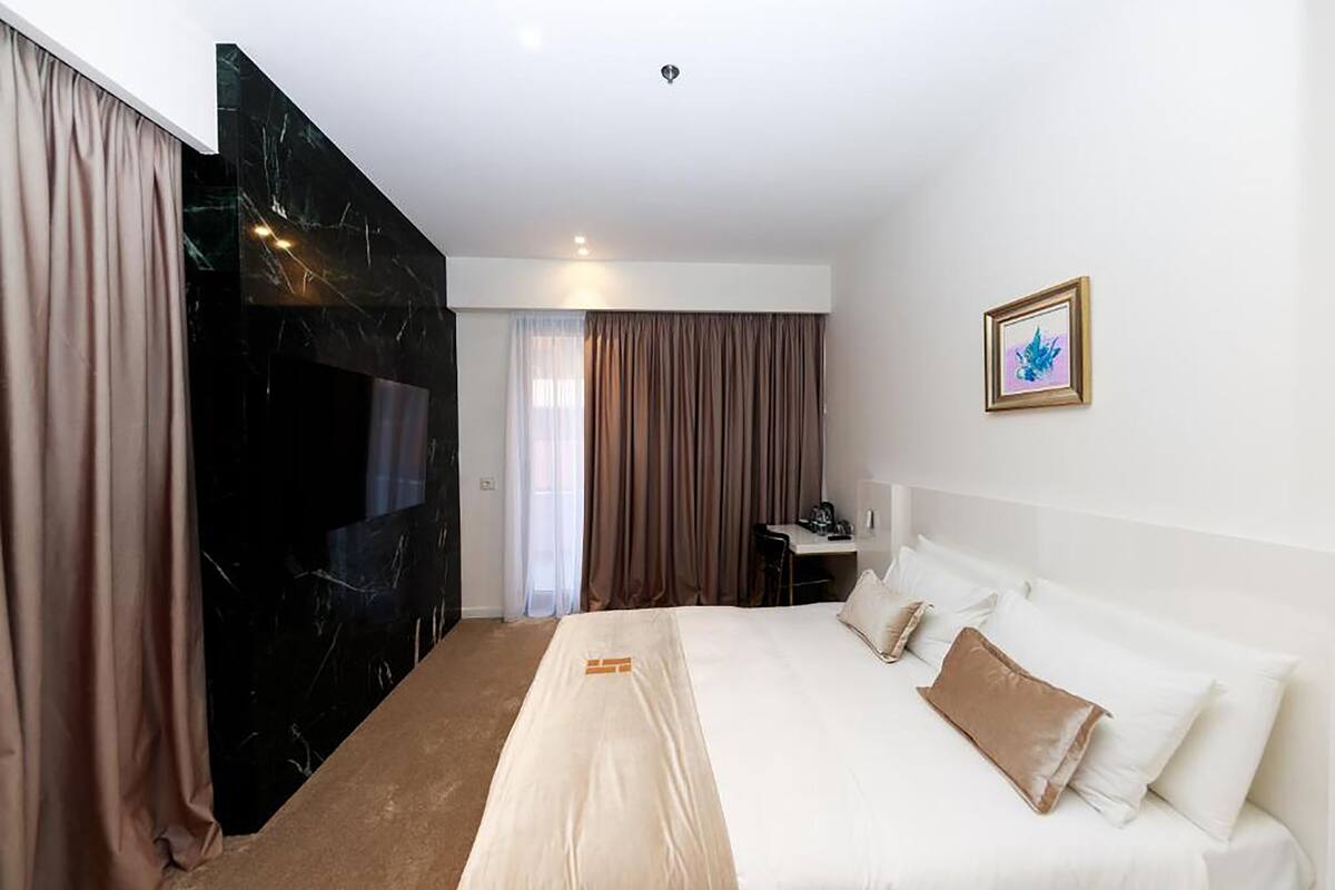 A hotel room with a bed, a desk, a chair, and a window with curtains.