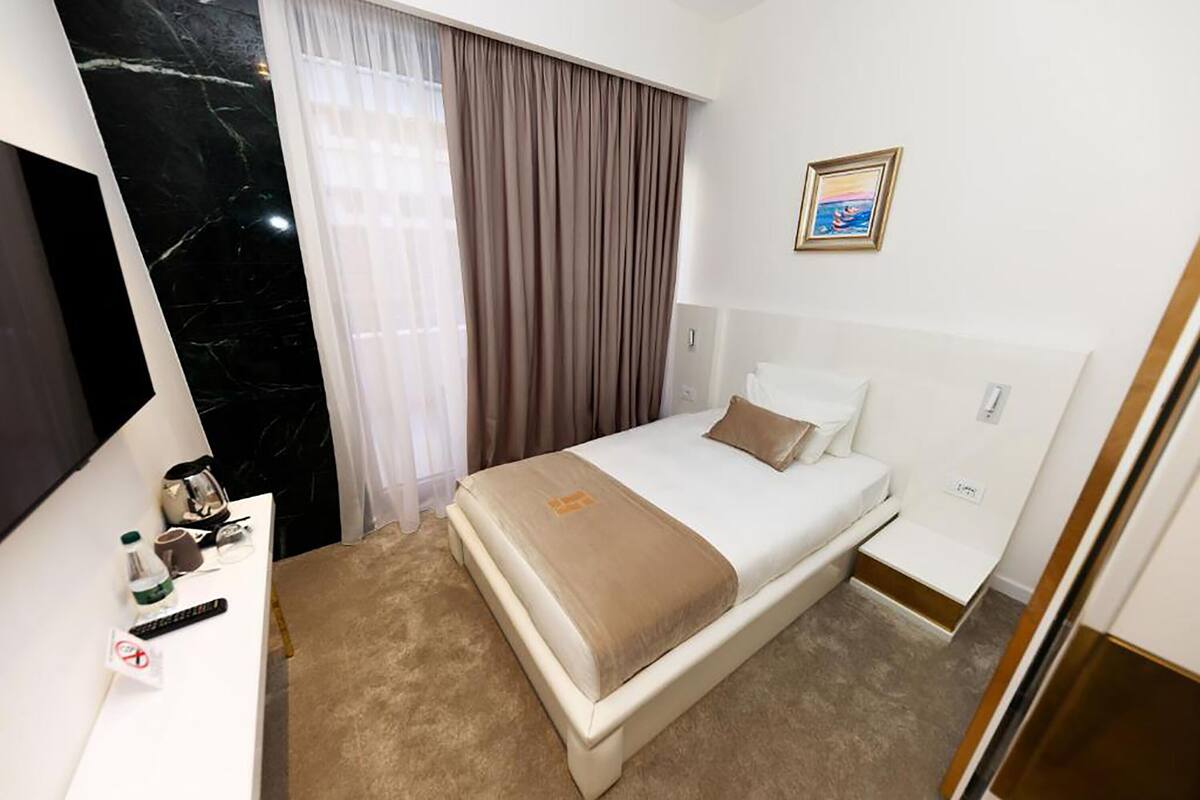 A hotel room with a bed, a desk, a television, a picture on the wall, and a window with curtains.