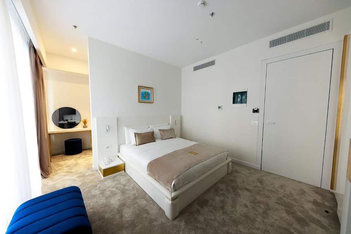 A hotel room with a large bed, a bedside table, a mirror, a wardrobe, and a small desk with a chair.