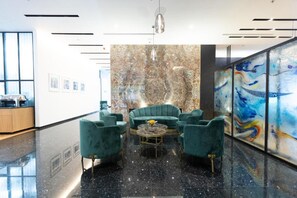 A lobby with a marble wall, teal armchairs, a coffee table, and artwork on the wall. - Habitat Hotel Tirana (Tirana)