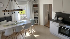 A modern kitchen with a built-in oven, a dining area with a table and chairs, and a view of the outdoors through a window. - Ferienhaus Hopfental (Kelheim)