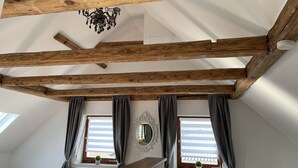 A room with exposed wooden beams, a chandelier, and two windows with curtains. - Ferienhaus Hopfental (Kelheim)