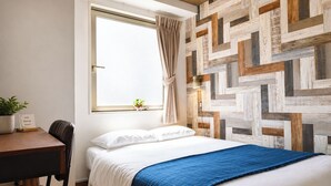 A bedroom with a bed, a desk, a chair, a window with curtains, and a wall with a geometric pattern. - Hotel Wan Osaka ebisu (Osaka)