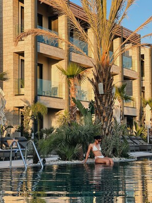A pool area with lounge chairs, a palm tree, and a building with balconies.
