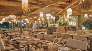 A restaurant with wooden tables and chairs, hanging lights, and a bar area in the background.