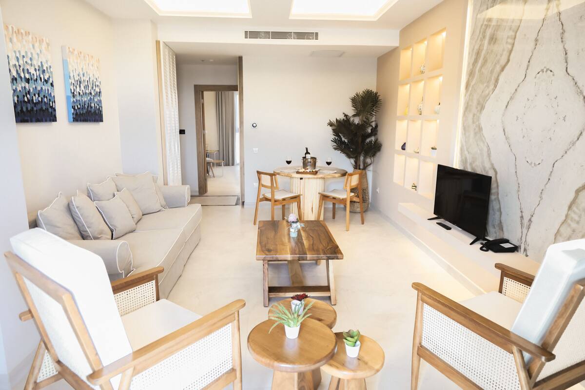 Una sala moderna con un sofá, sillas de madera, una mesa de centro, un televisor y una planta decorativa.