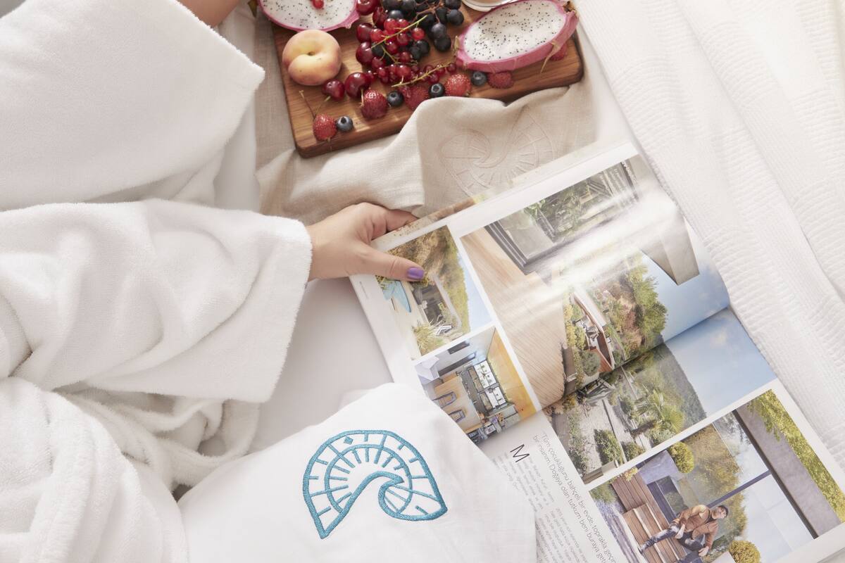 Una persona recostada en una cama con un libro y una bandeja de frutas.