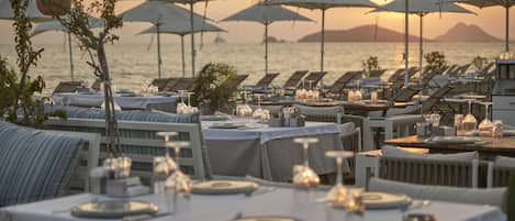 Ein Restaurant am Meer mit gedeckten Tischen, Sonnenschirmen für Schatten und Blick auf das Meer und vorgelagerte Inseln.