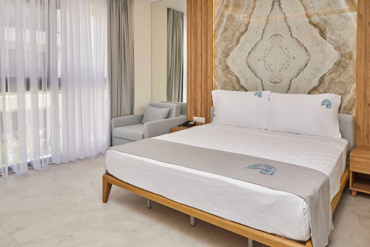 Una habitación de hotel moderna con una cama grande, un sofá gris y un cabecero de madera.