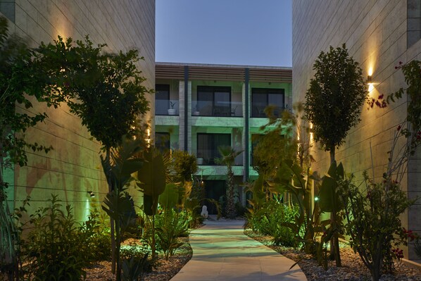 A pathway flanked by lush greenery and modern buildings with illuminated windows.