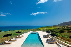 A pool area with lounge chairs and umbrellas, overlooking a coastal landscape. - Solitude, Chromatic Sunsets and Superior Sea Views (Rethymno)