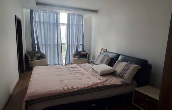 A bedroom with a bed, two nightstands, a dresser, and a window with curtains.