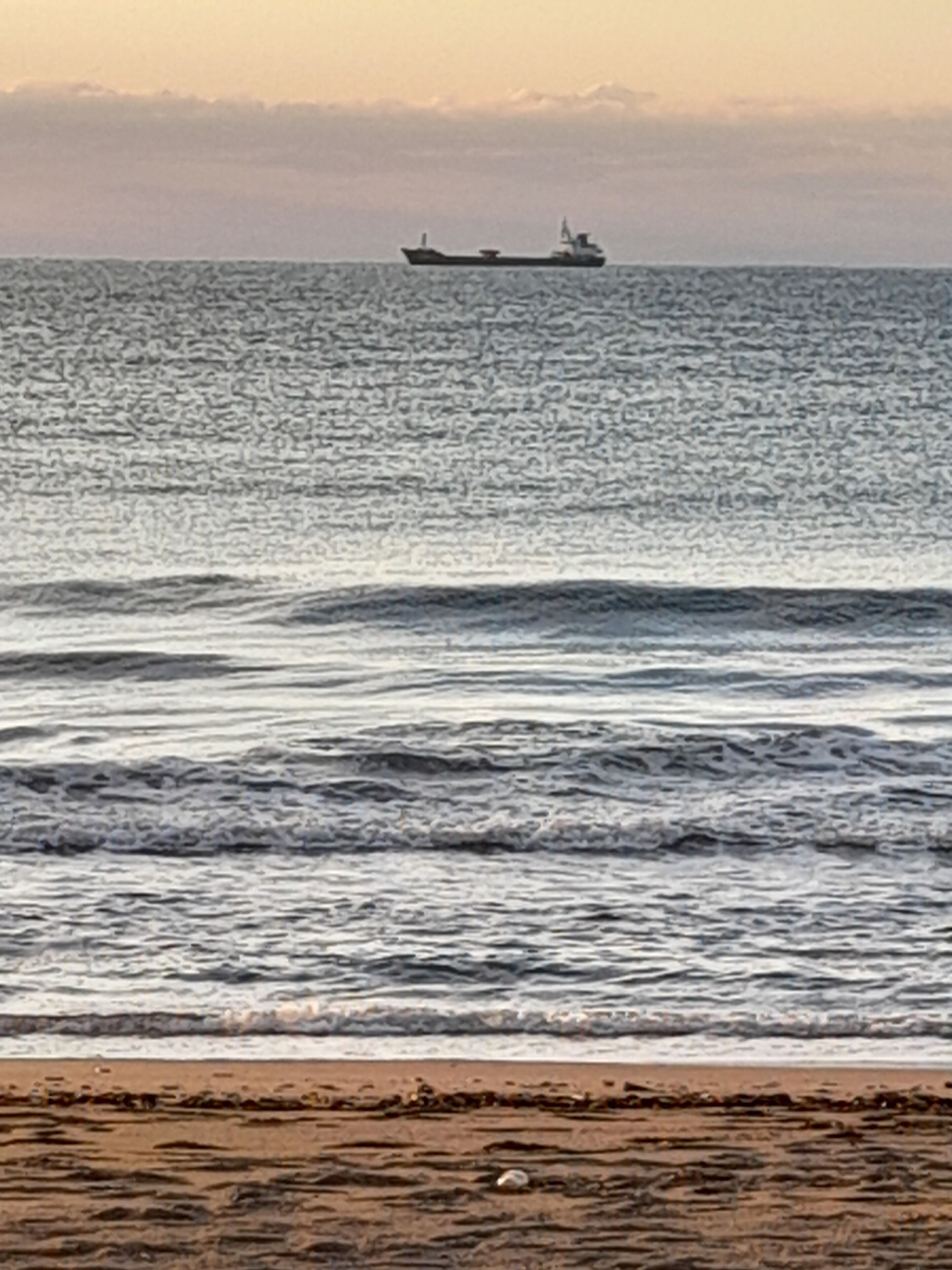 Una playa con olas y un barco a lo lejos.