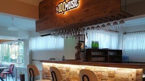 Un espace bar agrémenté d’une enseigne en bois sur laquelle on peut lire « 100 % MUSIQUE », de tabourets de bar, d’un comptoir avec des bouteilles et d’un mur en pierre.