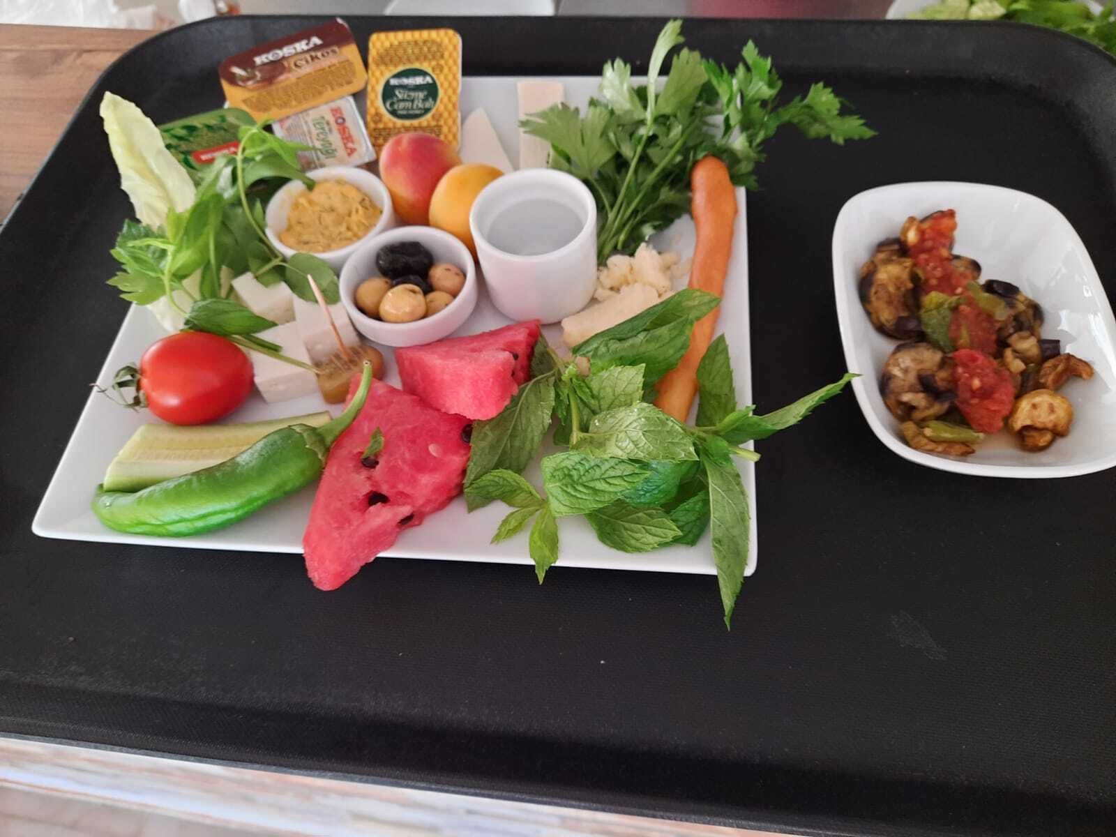 A tray with a variety of fresh vegetables, a tomato, a watermelon slice, and a small dish of roasted vegetables.