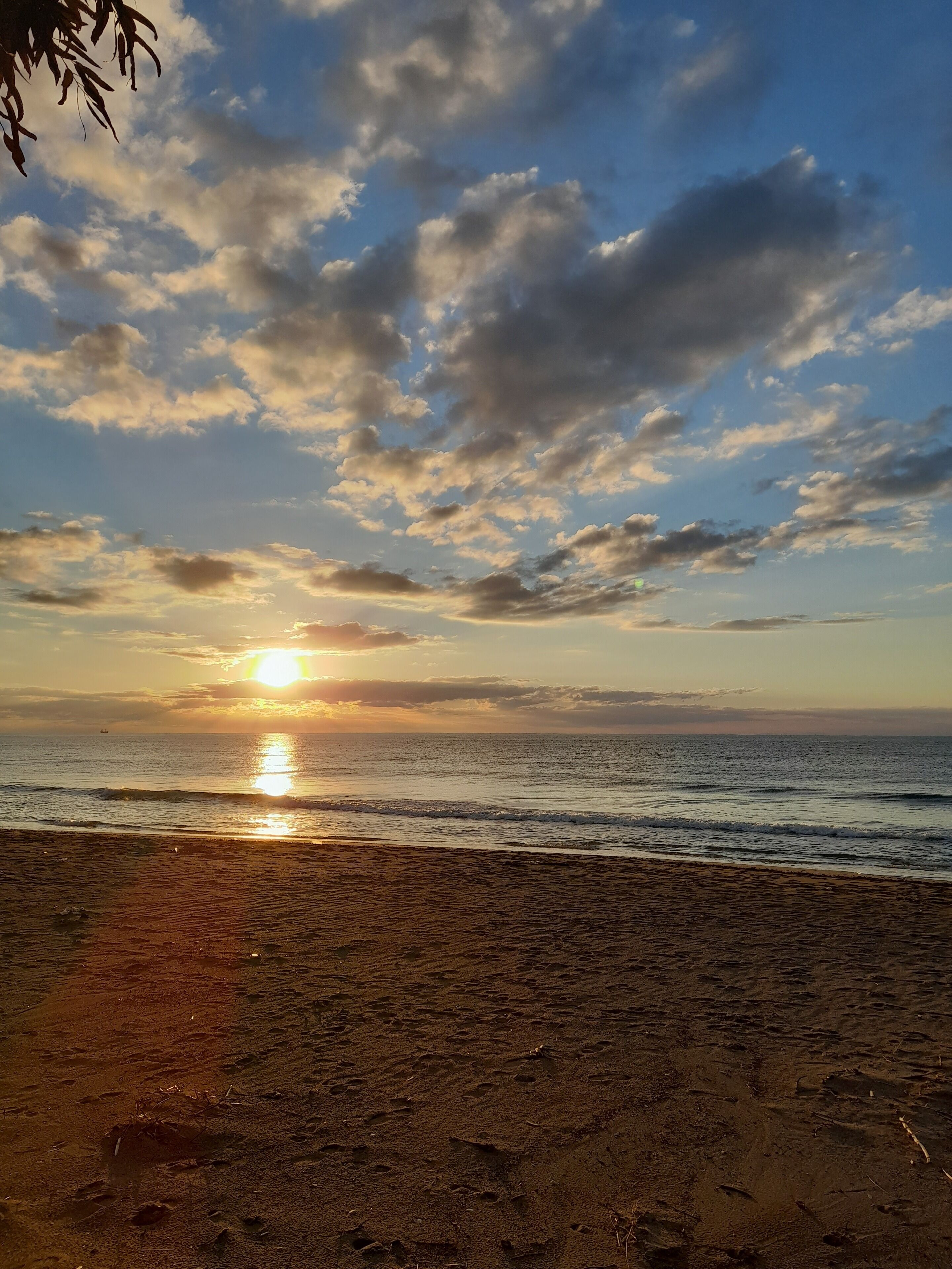Una playa con el sol poniéndose sobre el océano, creando una silueta de nubes en el cielo.