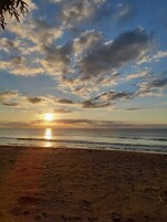 Una playa con el sol poniéndose sobre el océano, creando una silueta de nubes en el cielo.