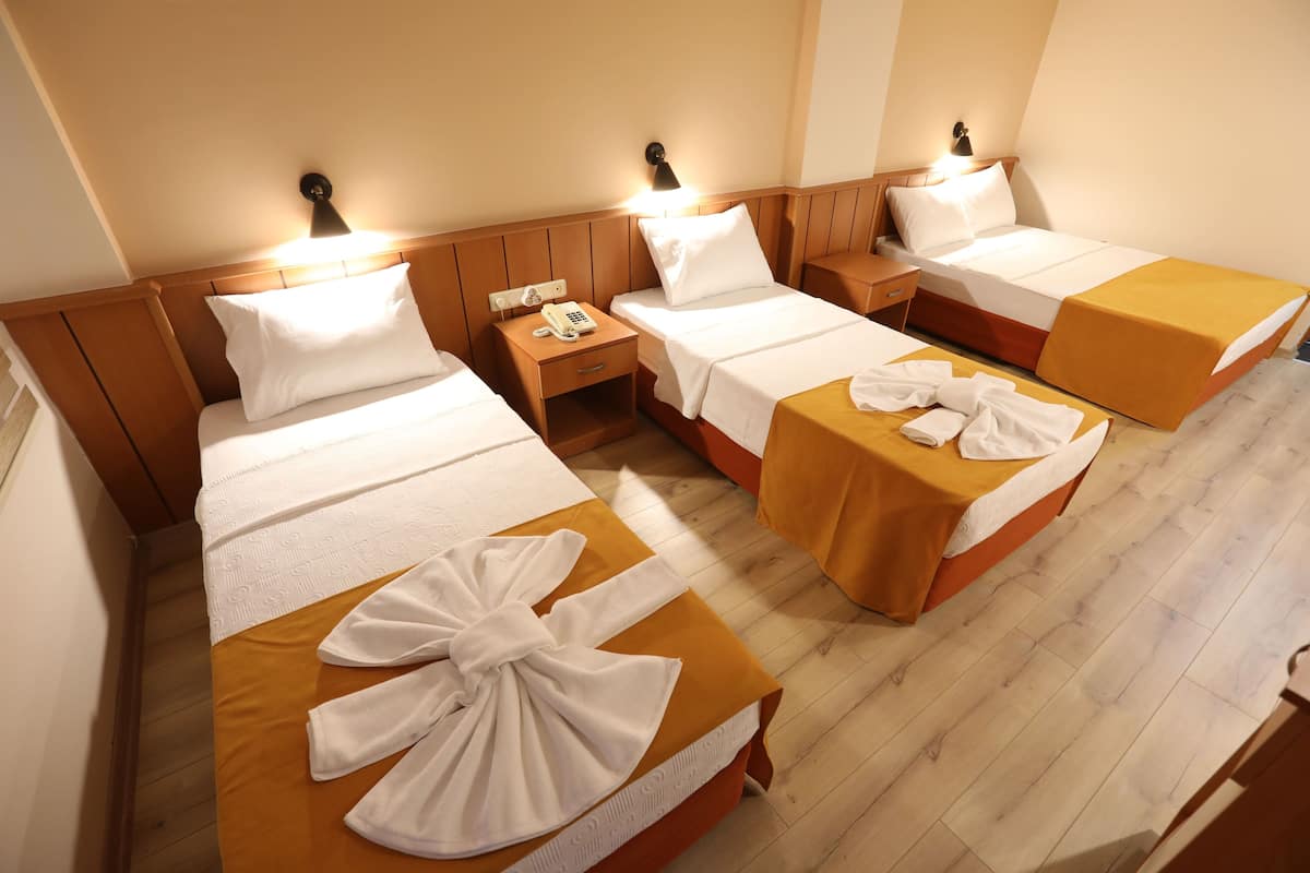 A hotel room with four single beds, each with a wooden headboard, white linens, and a yellow bedspread. There are bedside tables with lamps and a phone on one of them.