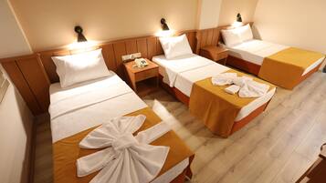 A hotel room with four single beds, each with a wooden headboard, white linens, and a yellow bedspread. There are bedside tables with lamps and a phone on one of them.