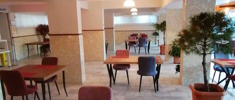 A spacious indoor area with multiple tables and chairs, a ceiling light fixture, and potted plants.