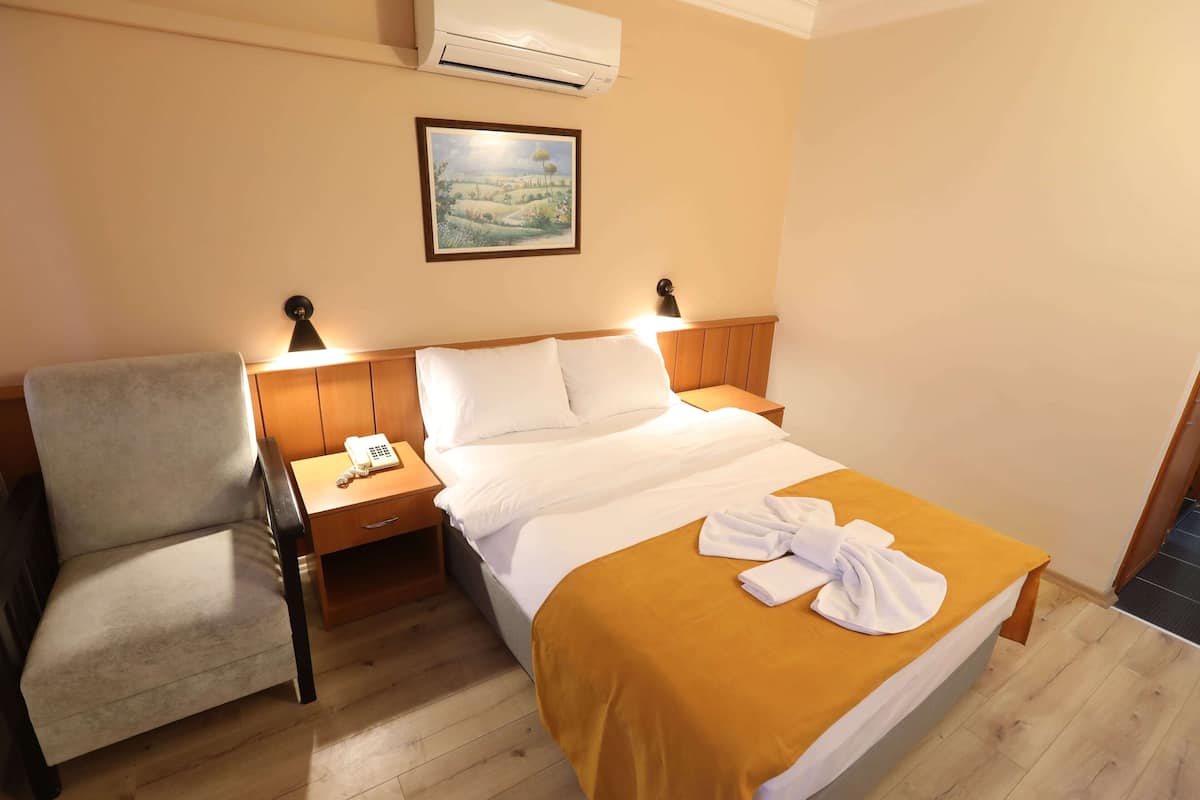 A hotel room with a bed, a chair, a bedside table with a lamp, and a painting on the wall.
