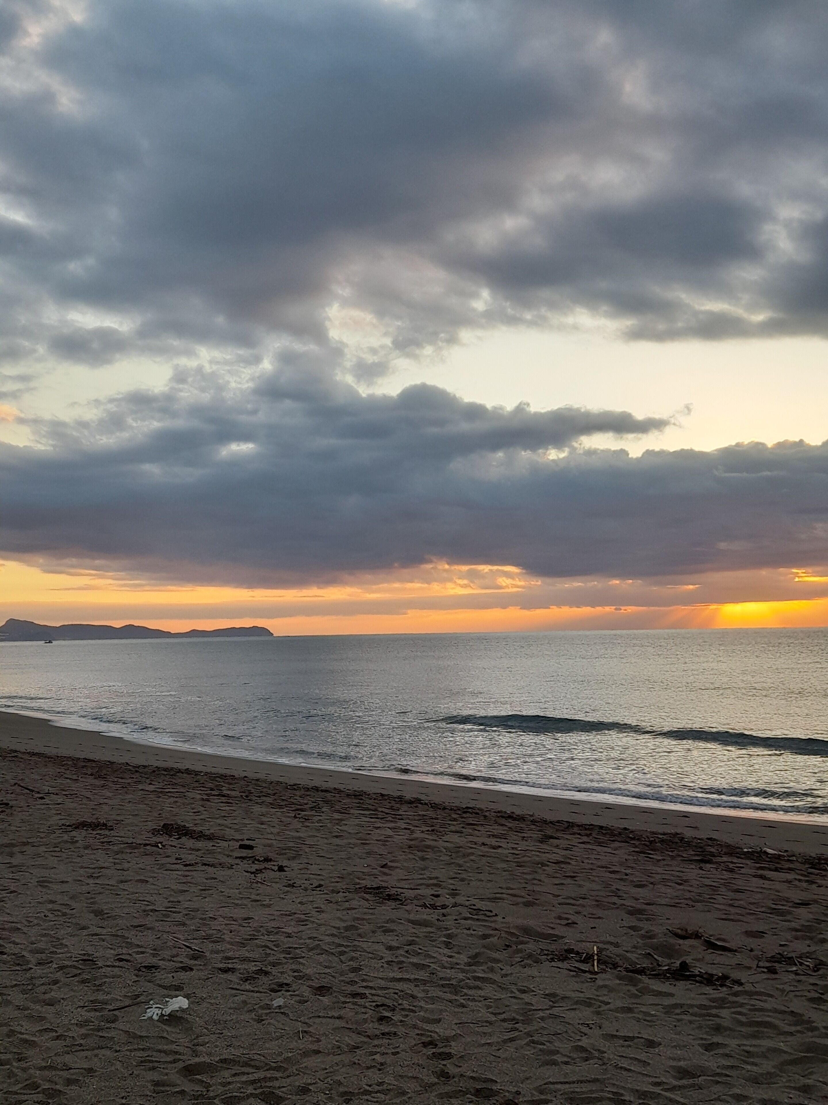Una playa con vista al océano y accidentes geográficos distantes bajo un cielo nublado.