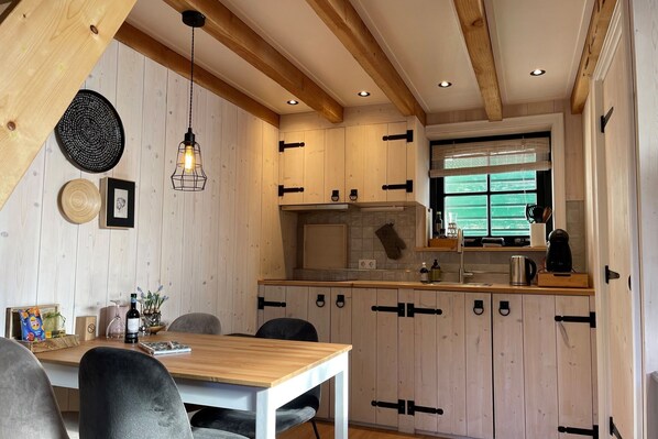 A kitchen with wooden cabinets, a dining table, and a hanging light fixture. - Inviting chalet in Monnickendam with garden (Monnickendam)