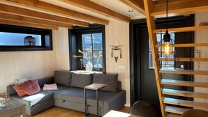 Un salon moderne avec un canapé d’angle gris, une petite table, un luminaire suspendu et une échelle en bois.