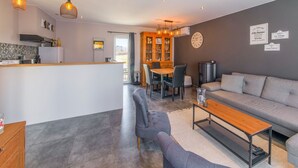 Un espacio habitable moderno con un sofá gris, una mesa de centro de madera y una zona de comedor con mesa y sillas de madera.