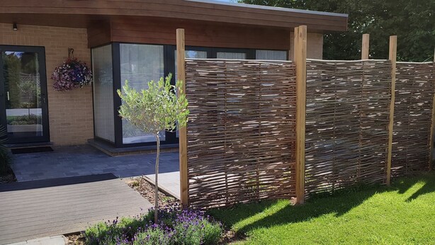 Una casa moderna con valla de madera, un árbol pequeño y flores púrpuras en el jardín.