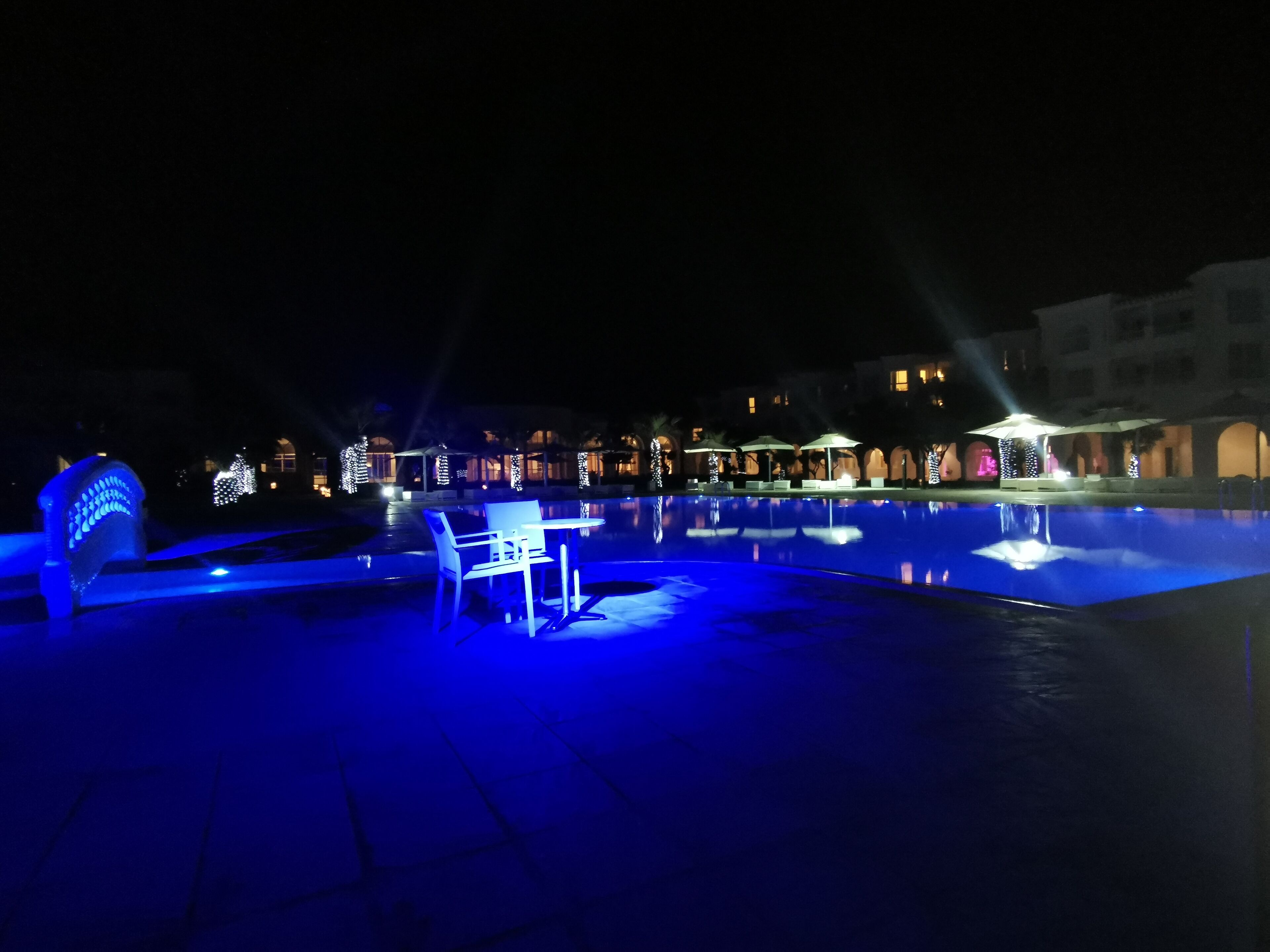 A nighttime pool area with illuminated seating and a fountain.