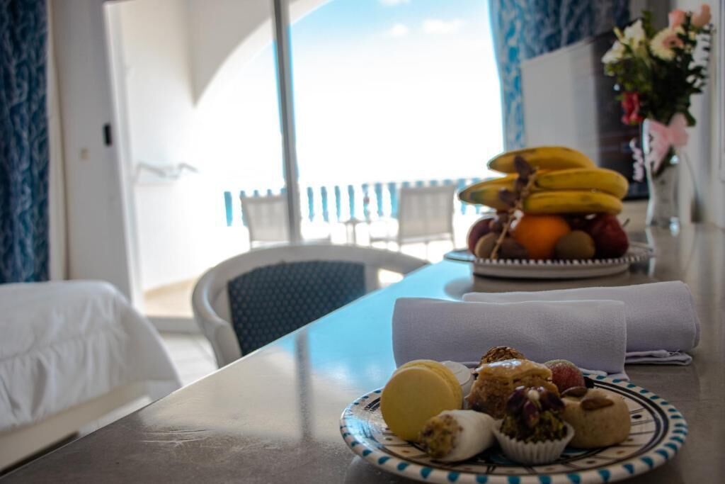 A dining table with a plate of food, a bowl of fruit, and a vase of flowers.