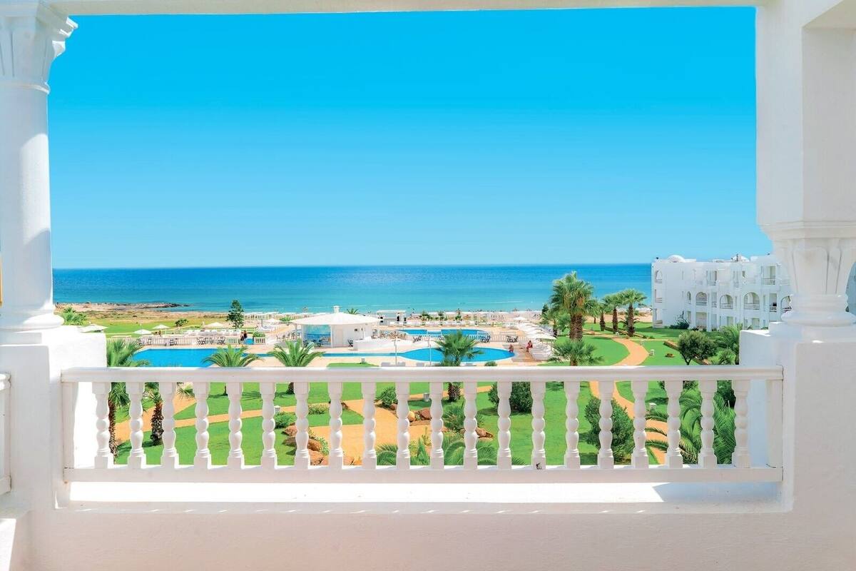 Un complex turístic amb piscina, palmeres i vista a l'oceà.