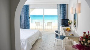 Une chambre d’hôtel avec un lit, un bureau avec une télévision et une vue sur la plage.