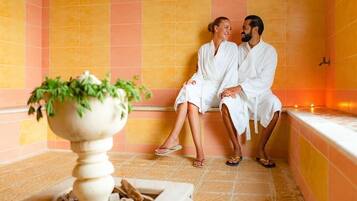 Guests can unwind in a serene spa setting with a warm ambiance, featuring a tiled floor and lush greenery.