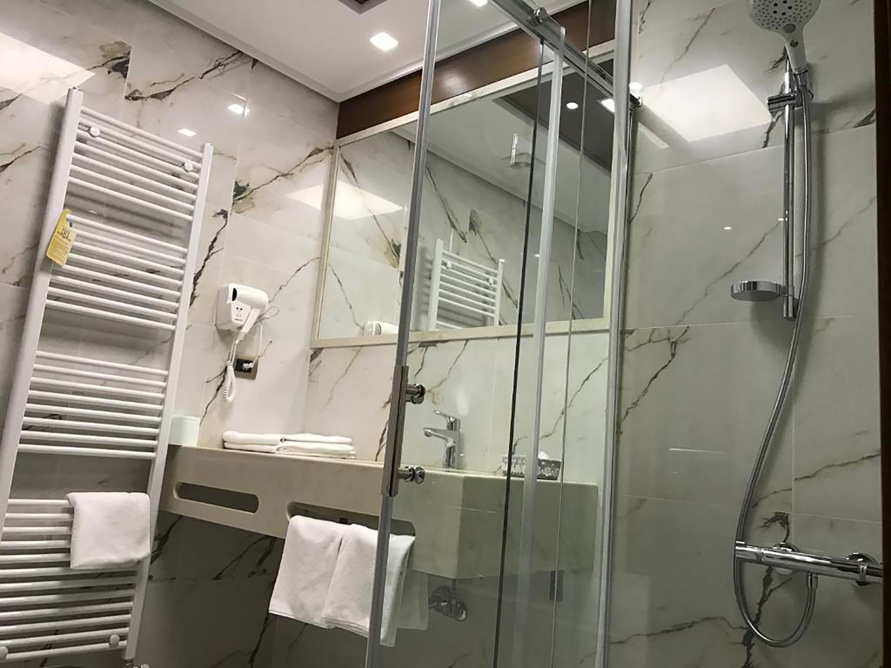 Un baño moderno con cabina de ducha de vidrio, toallero blanco y pared con azulejos de mármol.
