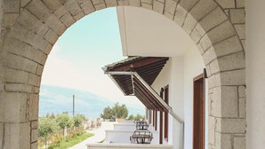 A stone archway leading to a balcony with a metal railing, overlooking a garden and a mountainous landscape. - Kerculla Resort  (Gjirokastër)