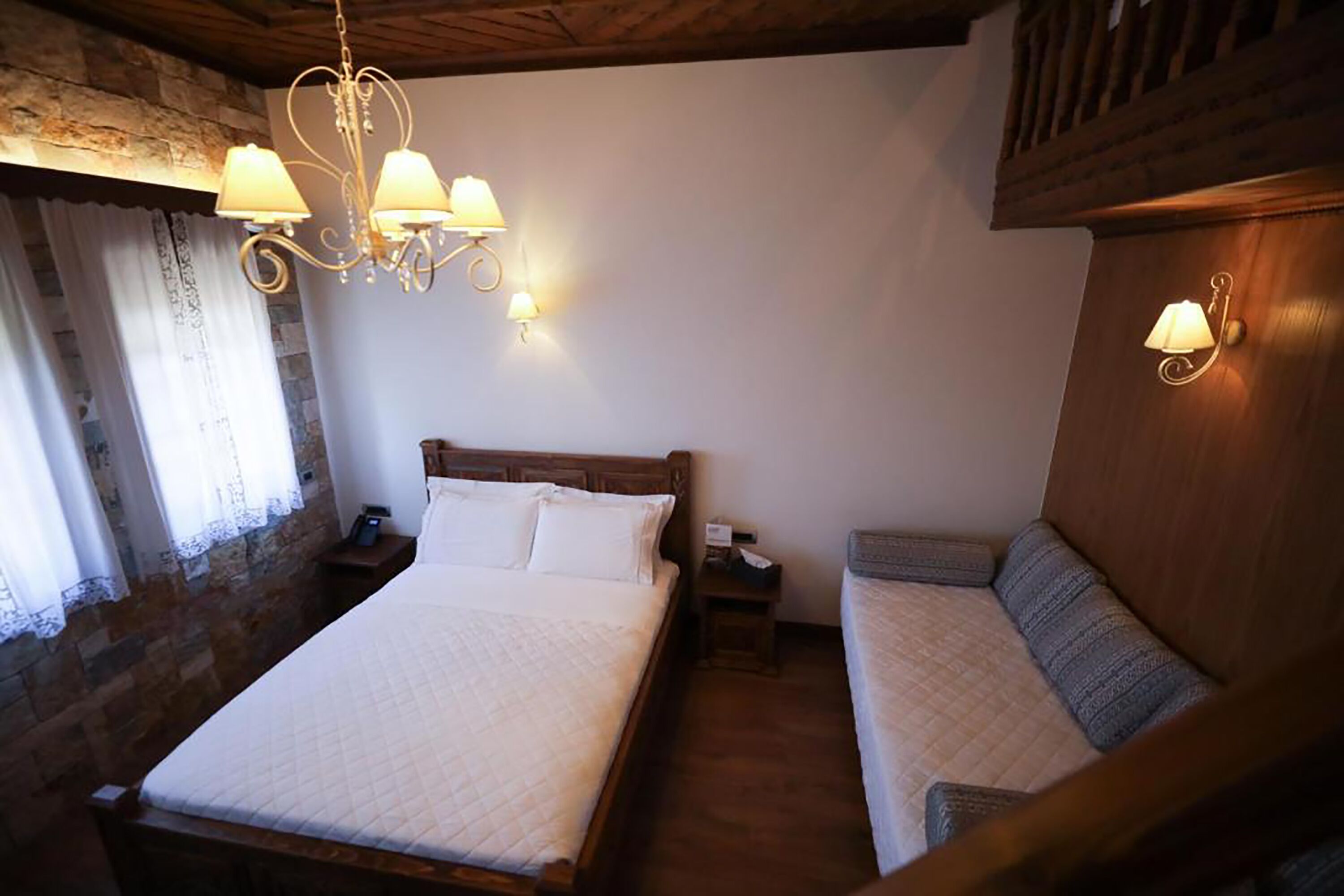 Un dormitorio acogedor con una cama grande, un sofá más pequeño y una araña.