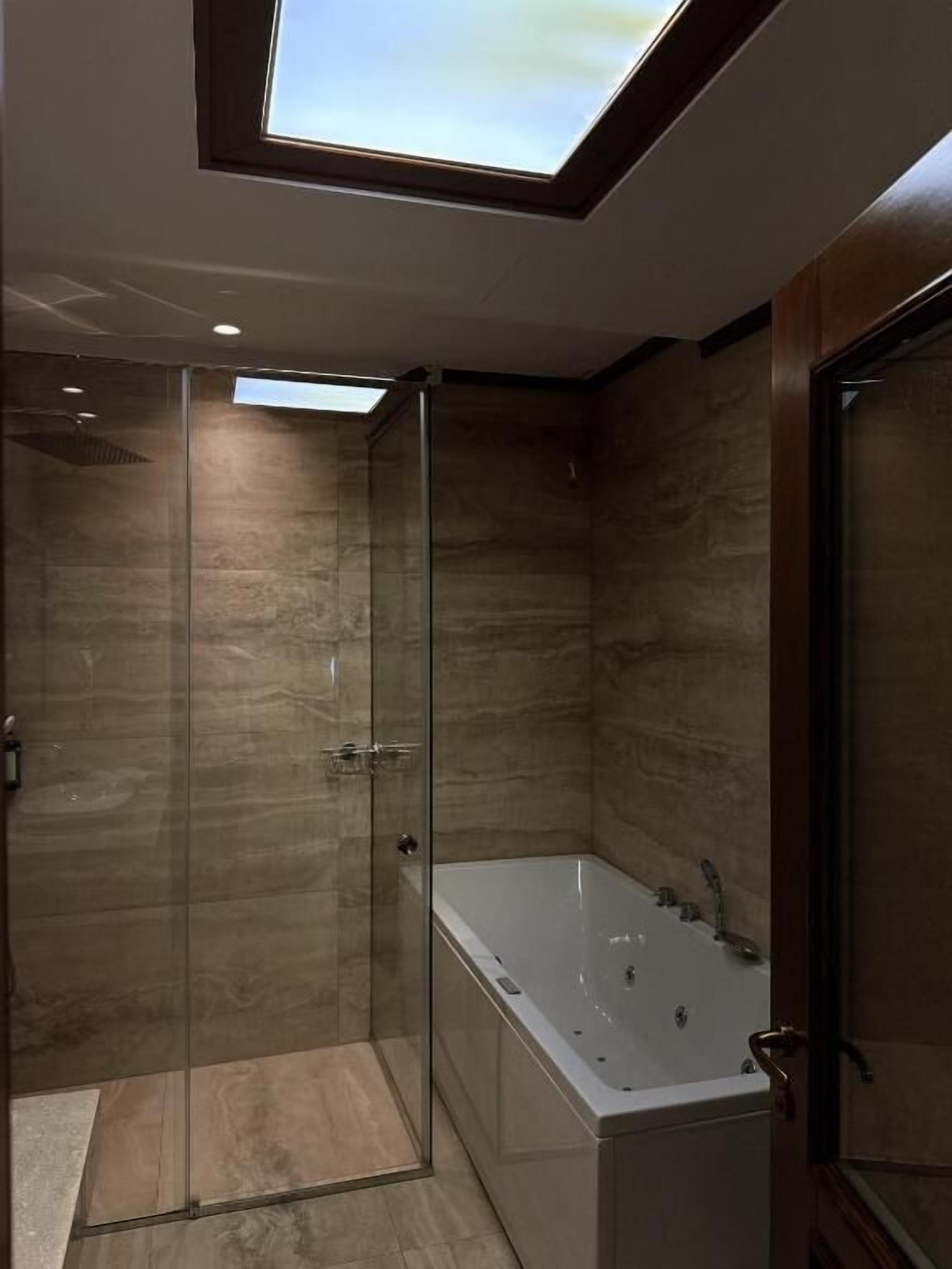 Une salle de bain moderne avec une douche à parois de verre, une baignoire sur pieds et un puits de lumière.