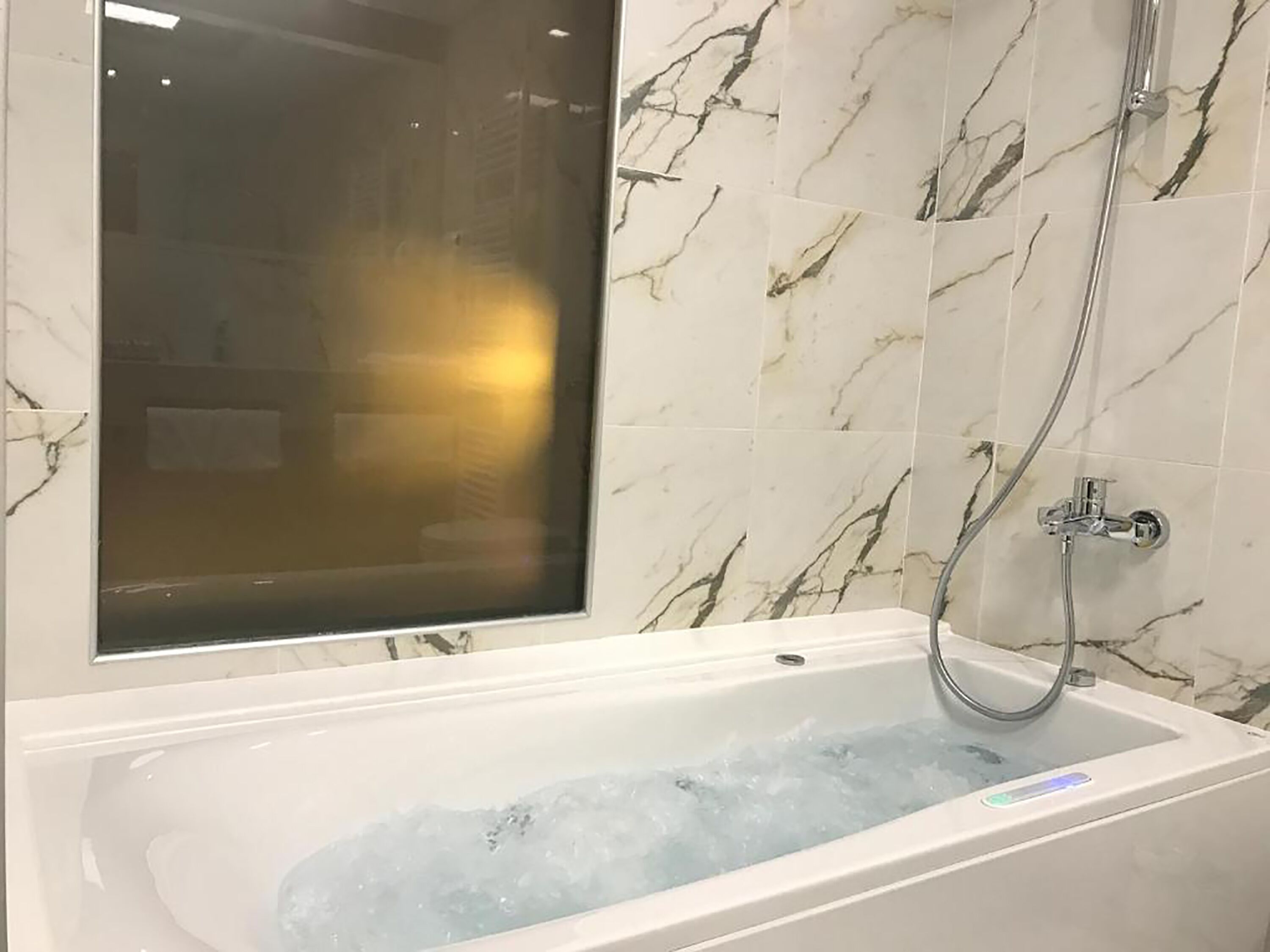 A modern bathroom with a bathtub filled with water, a glass shower enclosure, and marble-patterned walls.