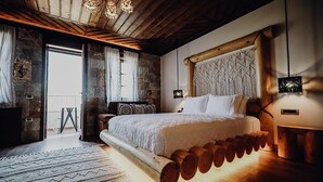 A bedroom with a large bed, wooden logs under the bed, a stone wall, and a wooden ceiling. - Kerculla Resort  (Gjirokastër)