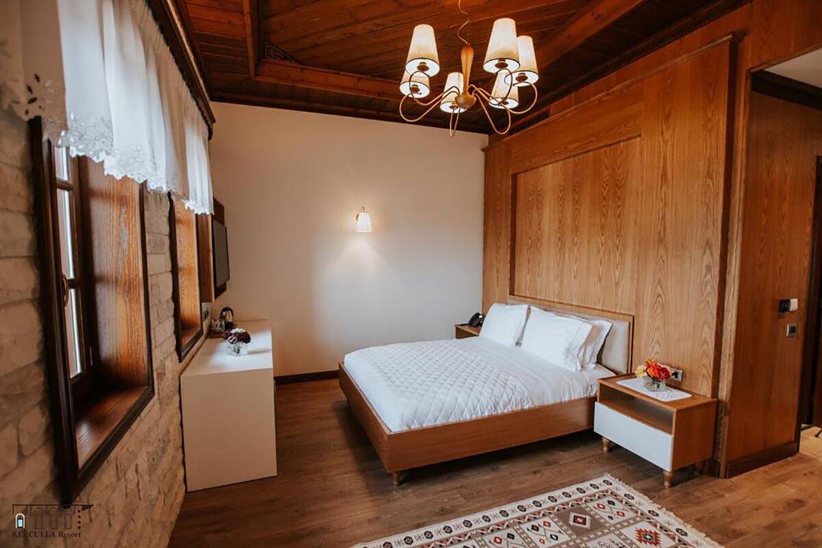 Un dormitorio con cama de madera, mesita de noche, lámpara de noche, candelabro y alfombra estampada.