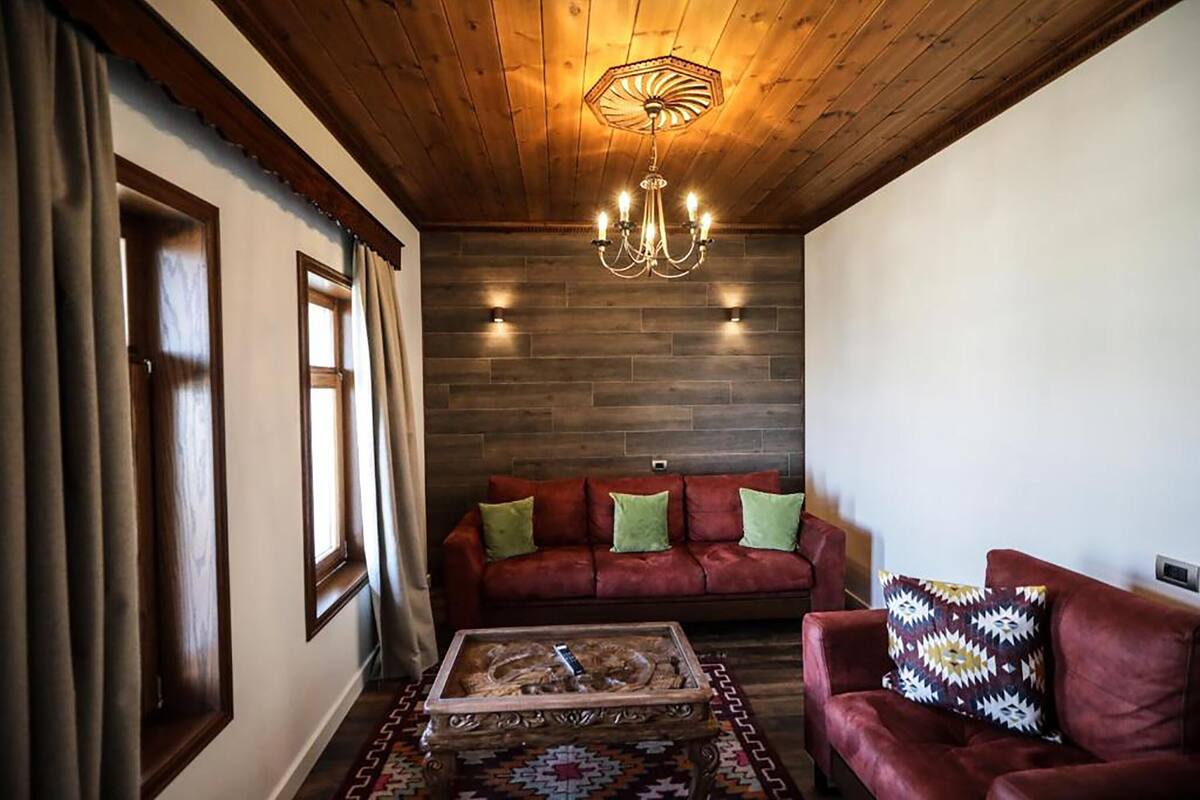 Un salón acogedor con techo de madera, un sofá rojo con cojines verdes y una mesa de centro estampada.