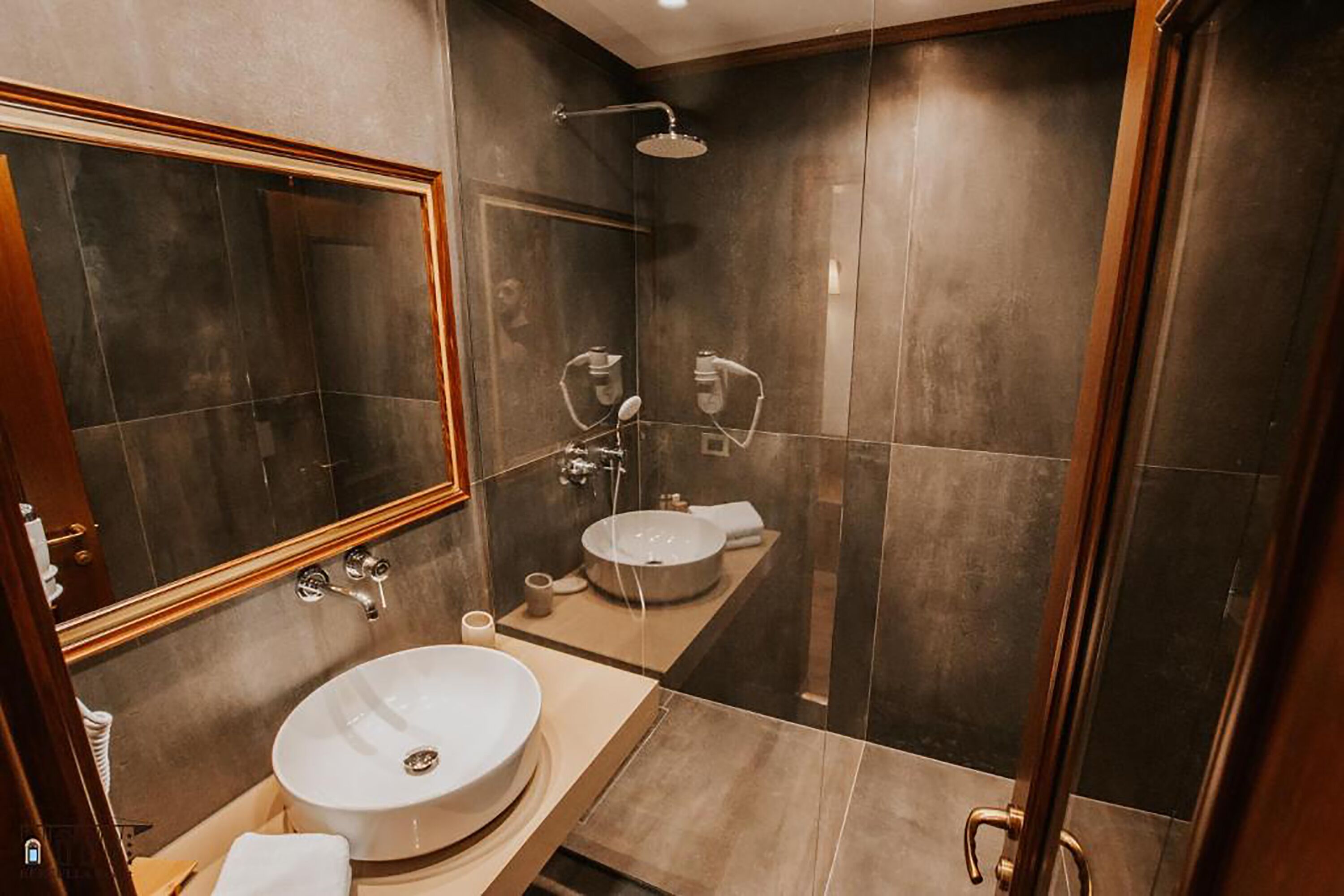 Une salle de bain moderne avec un grand miroir, un lavabo rond, une douche et un meuble-lavabo doté d’un porte-serviettes.
