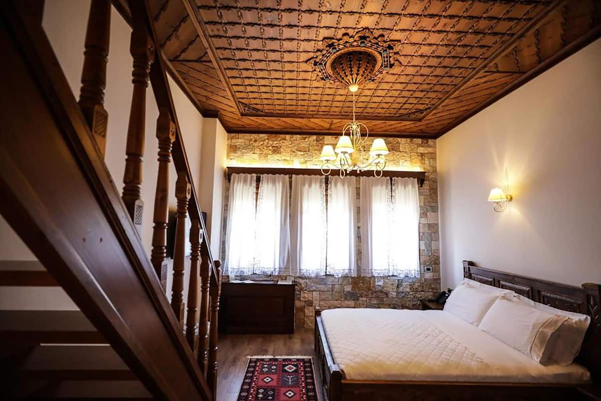 Un dormitorio con una cama de madera, pared de piedra, una araña y una escalera.