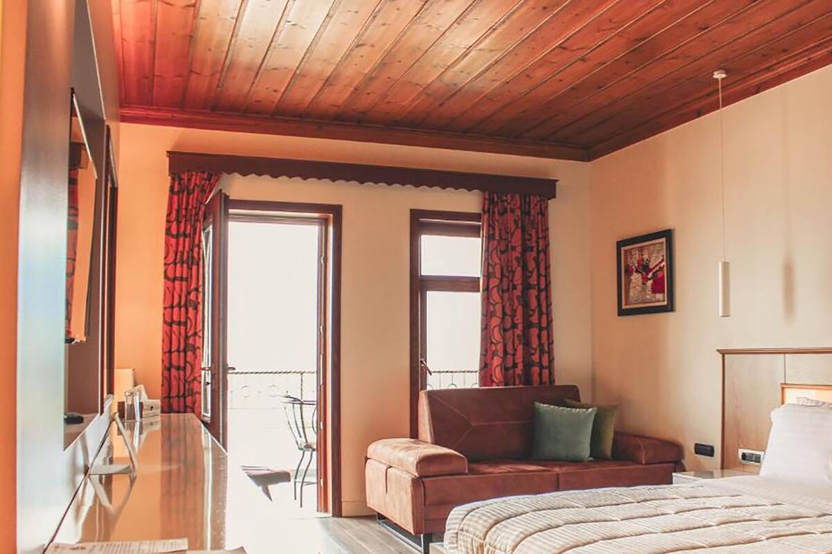 Un dormitorio con techo de madera, cama, sofá, escritorio y ventana con cortinas.