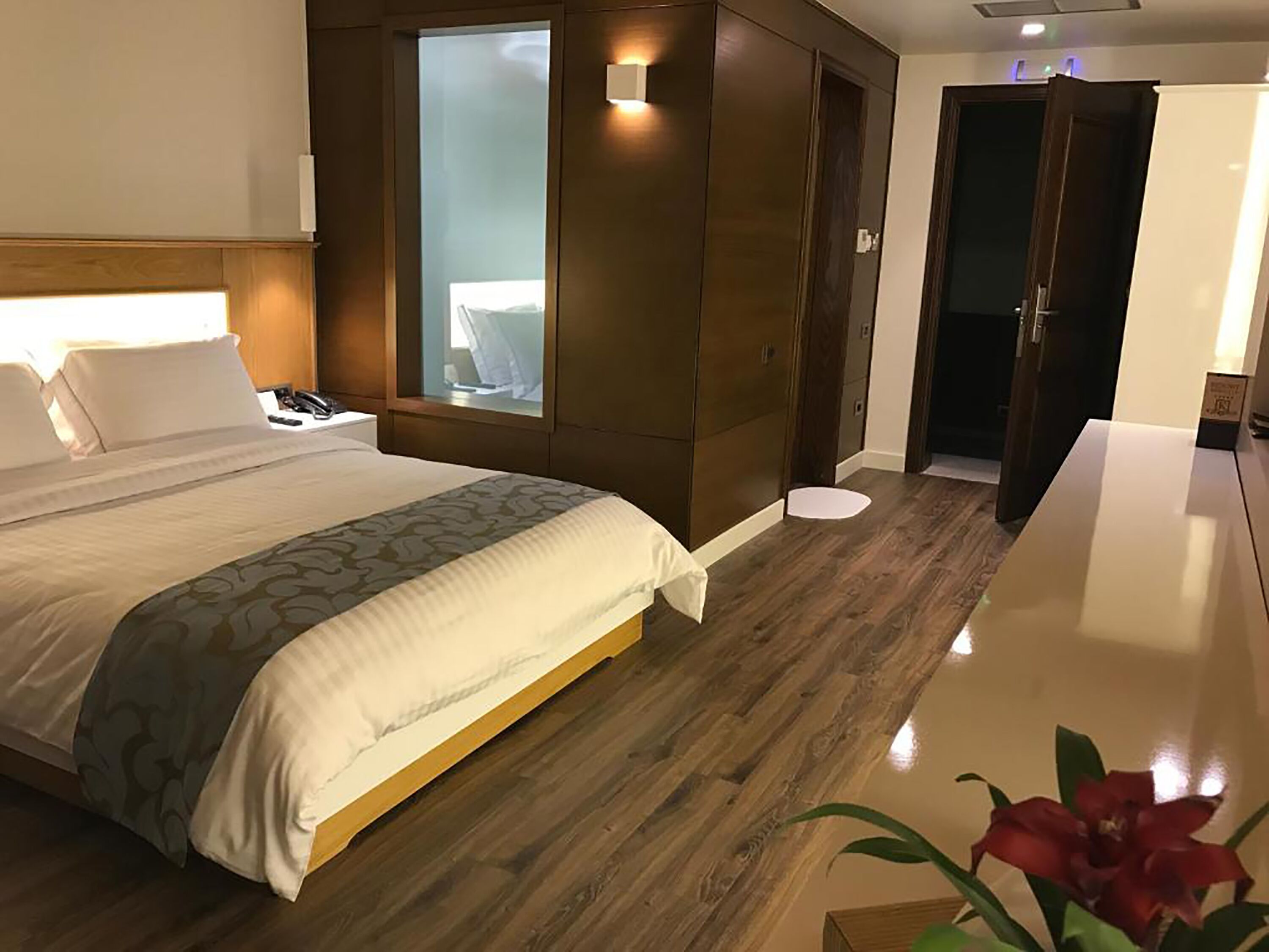 A hotel room with a large bed, a wooden wardrobe, a bedside table, and a small window.