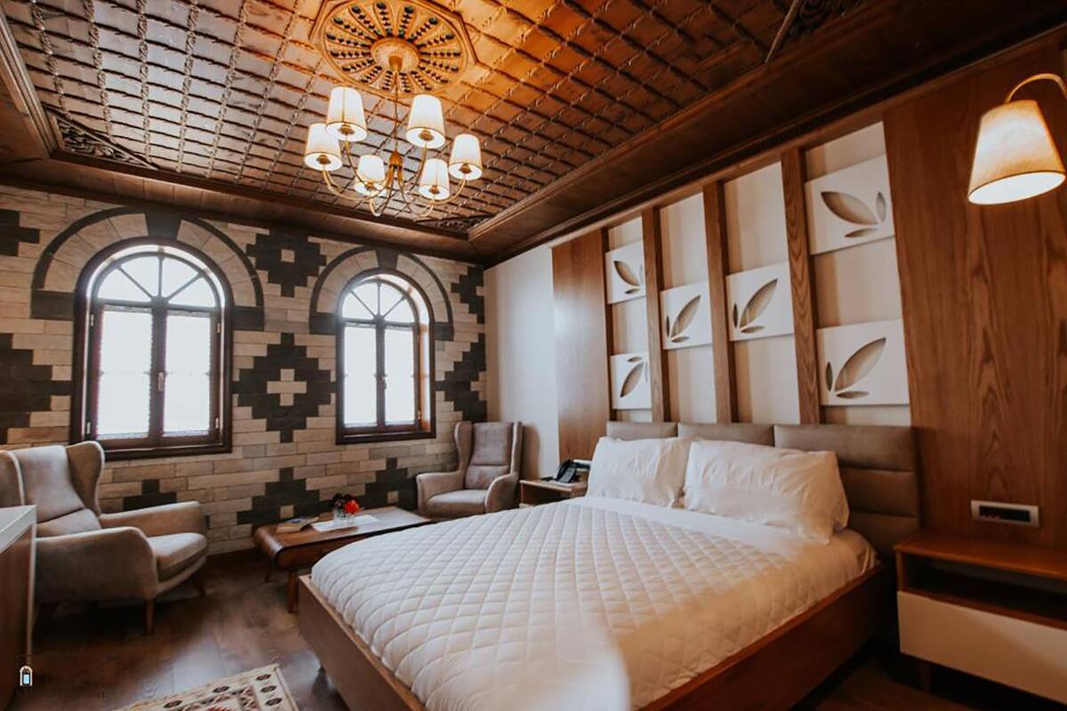 Un dormitorio con una cama grande, dos sillones, cabecera de madera, araña y paredes con estampado.